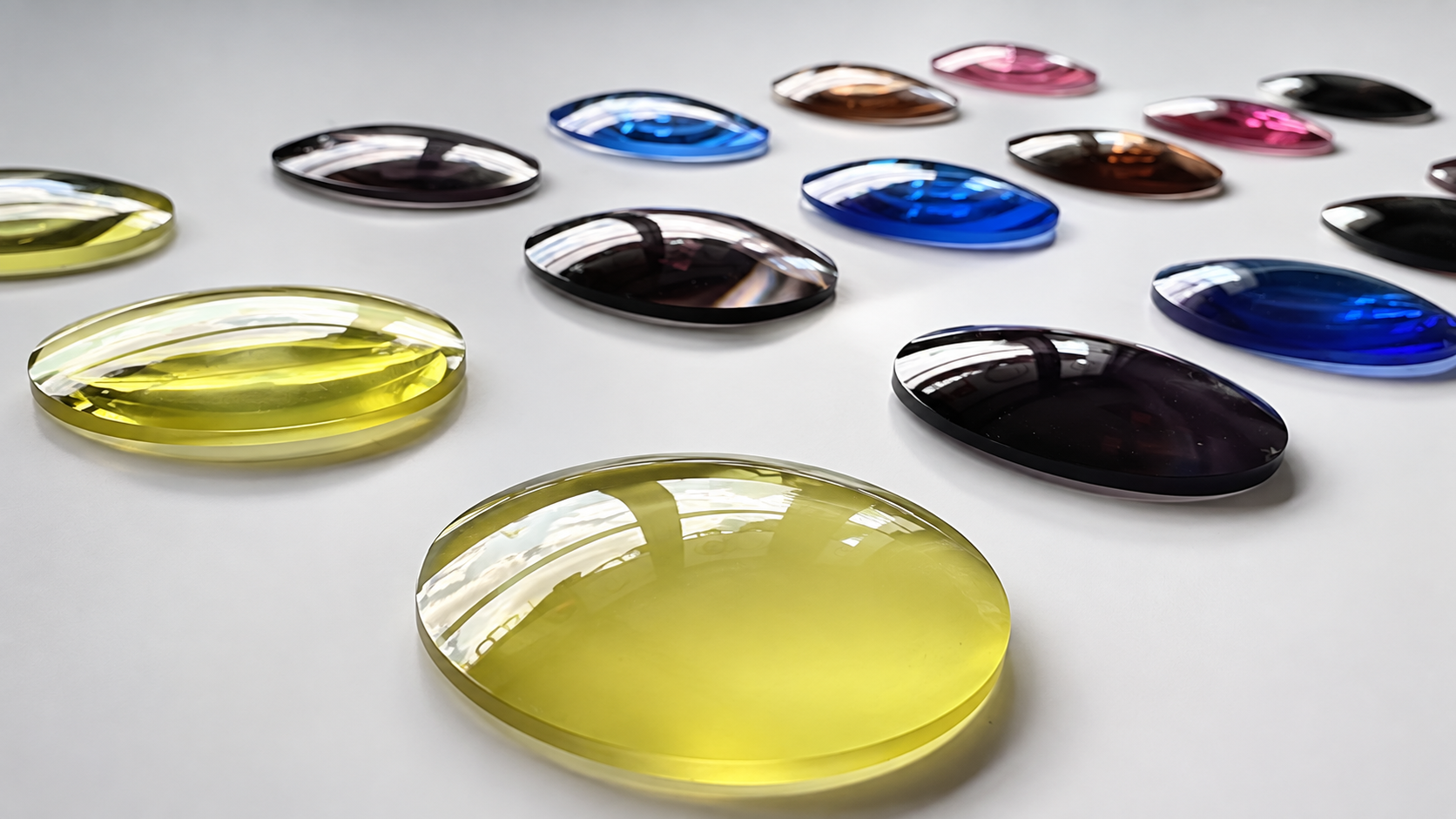 Finished tinted lenses in yellow, blue, purple, brown, and pink laid out on a white surface
